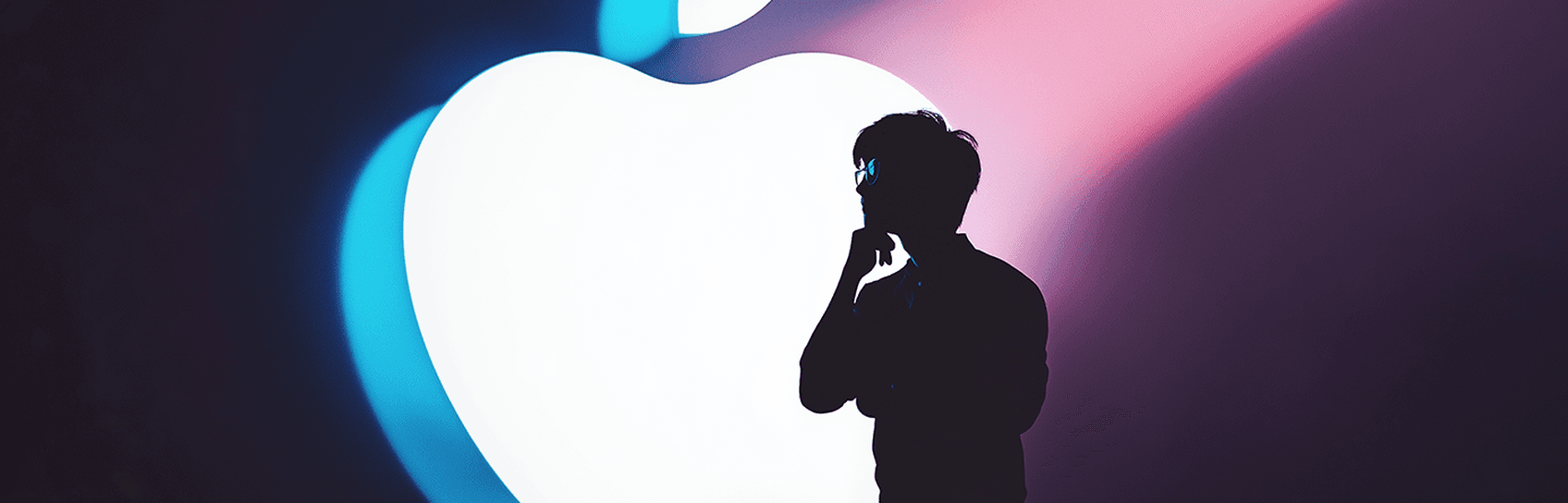 a silhouette of a man with a giant Apple logo behind up lit by studio lighting