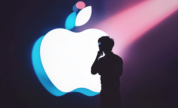 a silhouette of a man with a giant Apple logo behind up lit by studio lighting