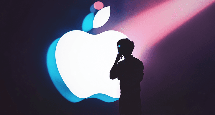 a silhouette of a man with a giant Apple logo behind up lit by studio lighting