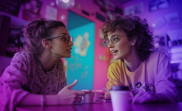 two young trendy ladies chatting over coffee in a vibrant pink coffee shop