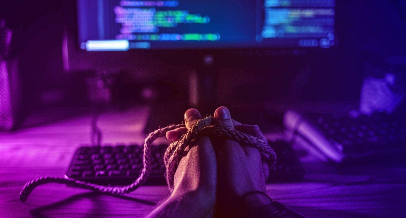 A web developers hands tied together in front of a screen with code on it in a dark room