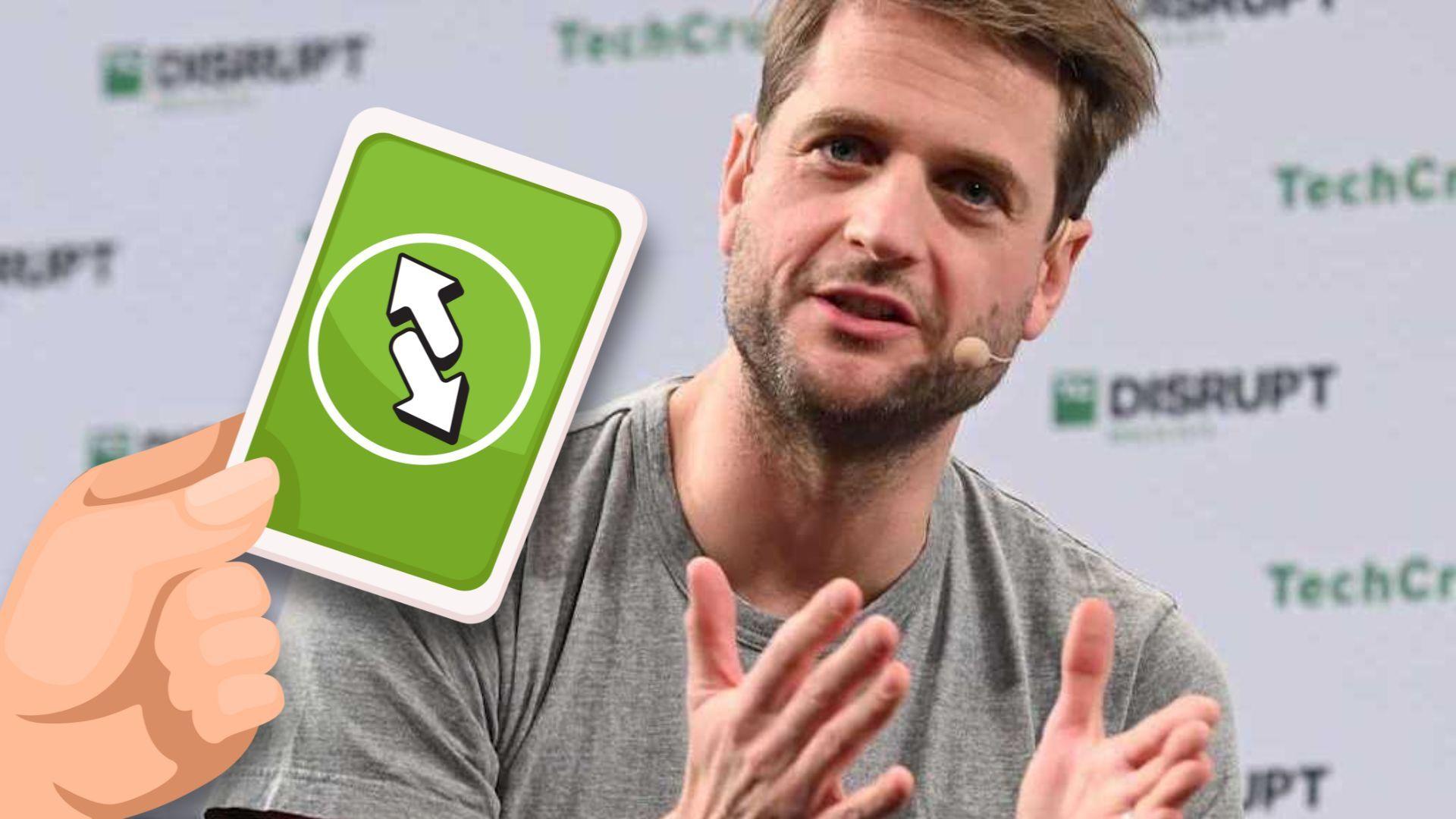 A person speaking on stage with a microphone, gesturing with hands. A green reverse card emoji is overlaid on the image.