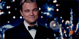 Leonardo DiCaprio raising a champagne glass whilst fireworks go off in the background.