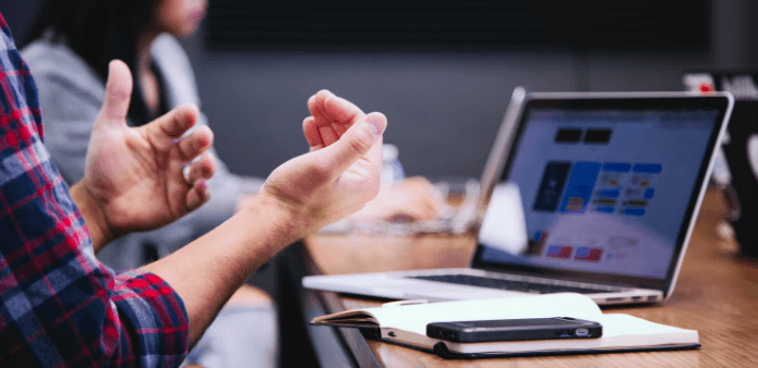 Man at a meeting table with hands apart explaining something very important.